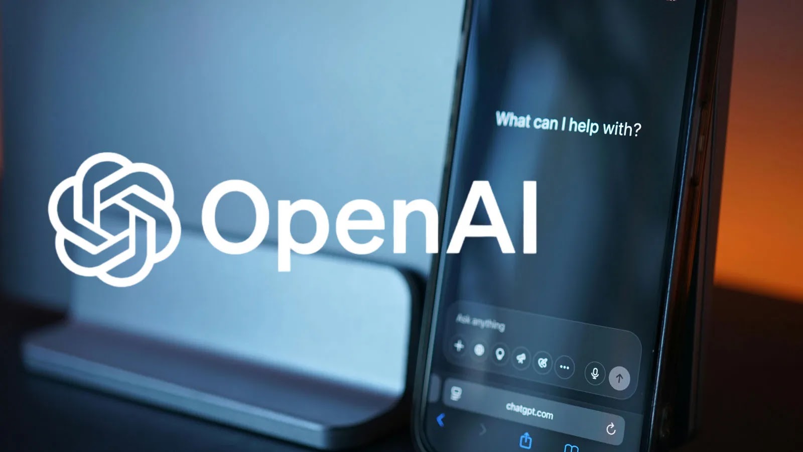 New DHS Warrant Asks…_imresizer A smartphone displaying a chat interface with the text What can I help with? is in the foreground, alongside a large white OpenAI logo and text, with a blurred background.