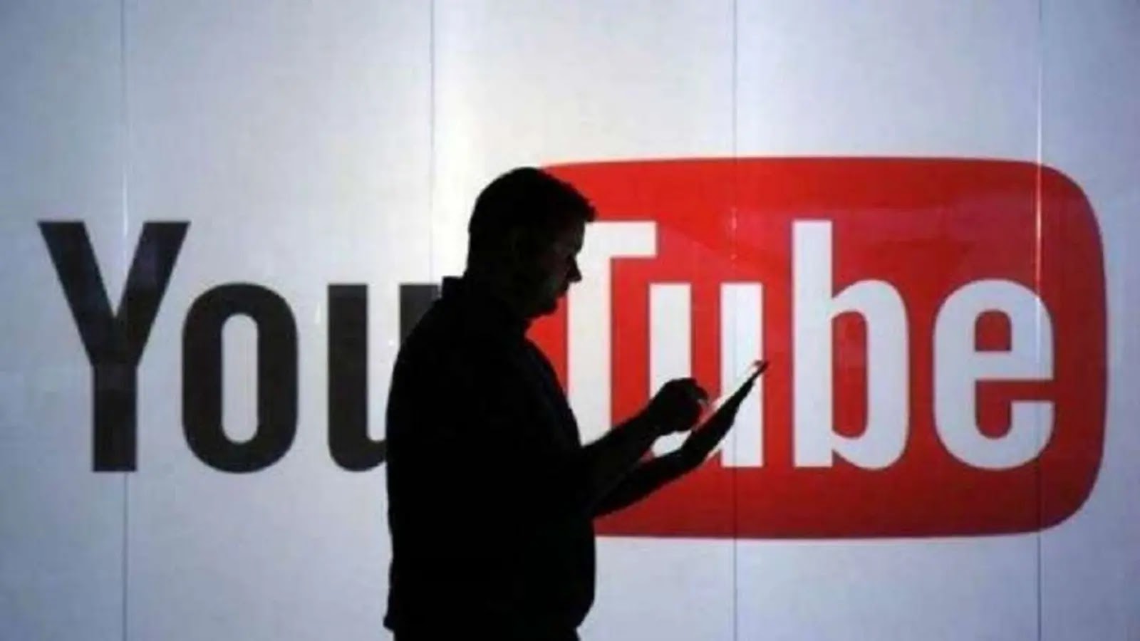 YouTube Down A silhouette of a person using a tablet in front of a large illuminated YouTube logo on a wall.