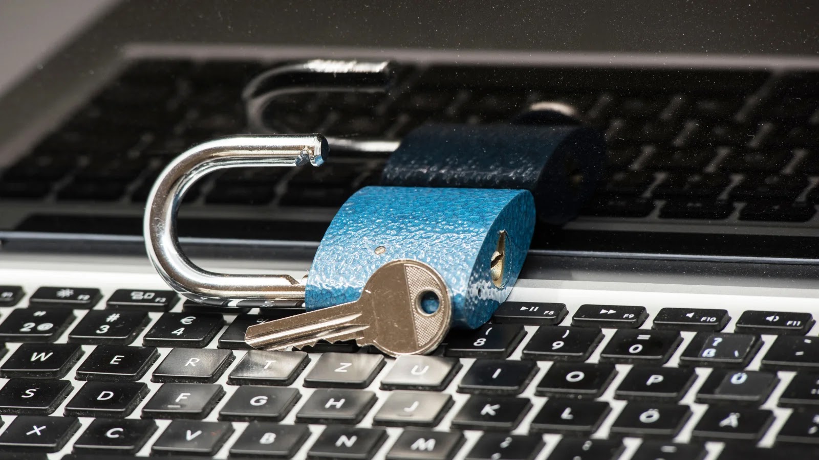 A blue unlocked padlock and a silver key rest on a laptop keyboard, symbolizing cybersecurity or data protection concepts.