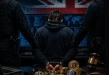 A person in handcuffs sits at a computer with digital screens, flanked by two officers. In front are cryptocurrency coins and a gavel. A large British flag hangs in the background.