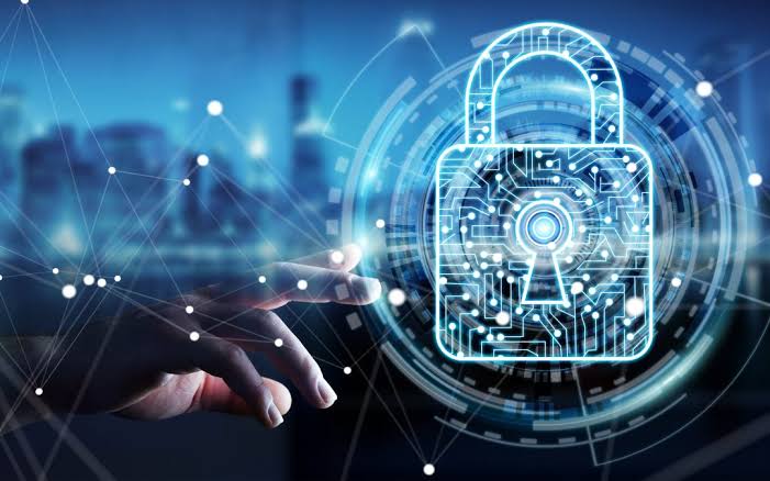 PQC A hand reaches toward a glowing digital padlock, symbolizing cybersecurity and data protection, with a network of connected lines and a blurred cityscape in the background.